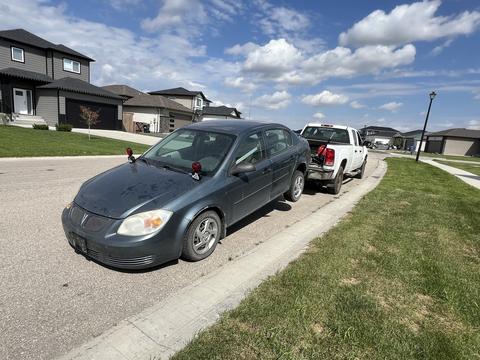Scrap Metal Pickup Truck Towing a Car in Residential Area